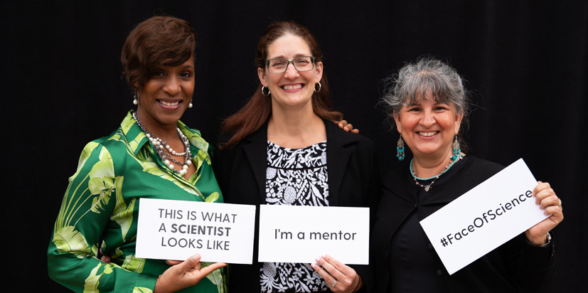 Three people who are each holding a sign. Each sign says: This is what a scientist looks like, I'm a mentor, and hashtag FaceOfScience.